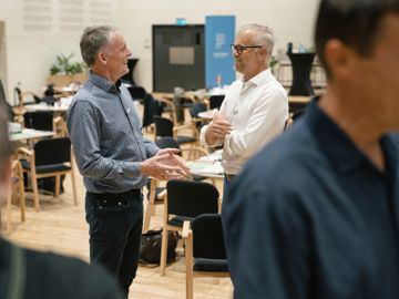 Tillidsrepræsentanterne Allan Danielsen-Boe og Brian Sørensen står på gulvet i en sal i samtale