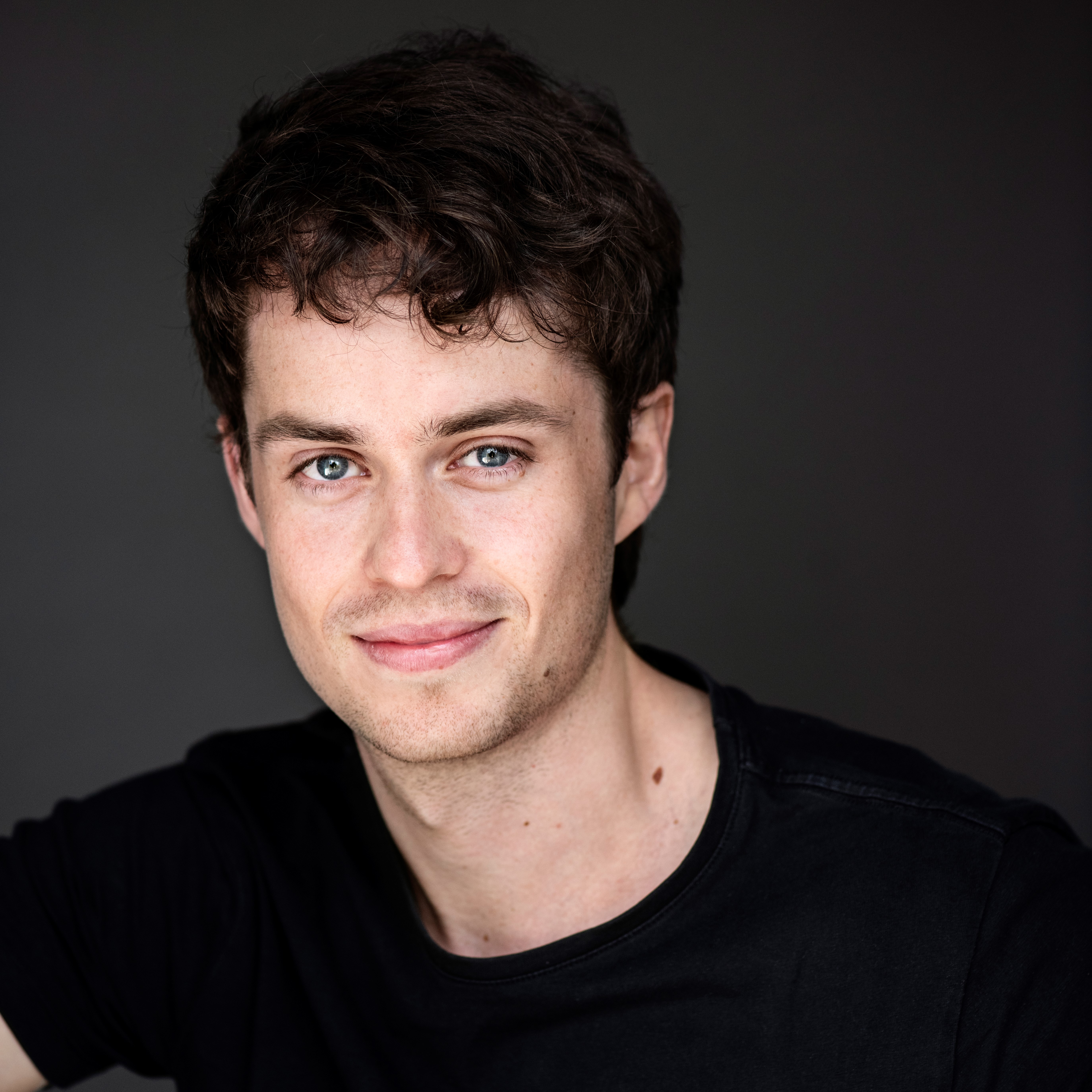 nicklas ser i kameraet smiler på mørk baggrund sort t-shirt