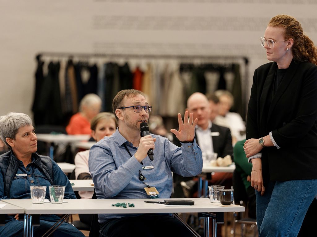 tre mennesker i forgrunden. en siddende med mikrofon
