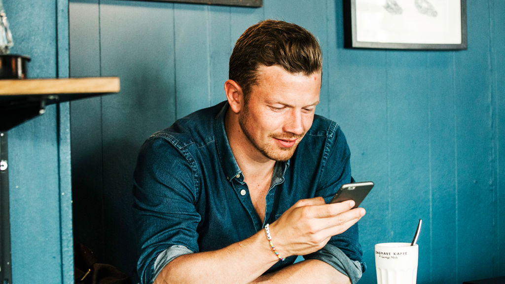ung mand sidder på cafe og kigger på sin telefon