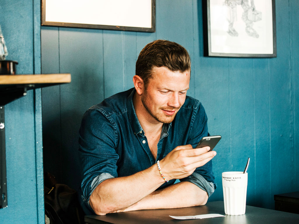 ung mand sidder på cafe og kigger på sin telefon
