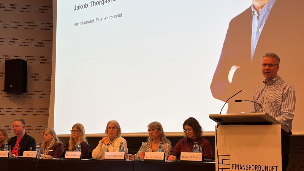 Næstformand i Finansforbundet Jacob Thorgaard på talerstolen, 6 personer siddende i panel i baggrunden.