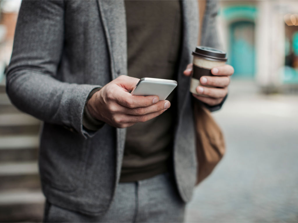 et menneske holder sin telefon og en kaffe i hånden