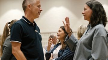 Tillidsrepræsentanterne Louise Fensten og Henrik Attermann står på gulvet i en sal i samtale. I baggrunden ses tillidsrepræsentant Maia Willaume-Jantzen