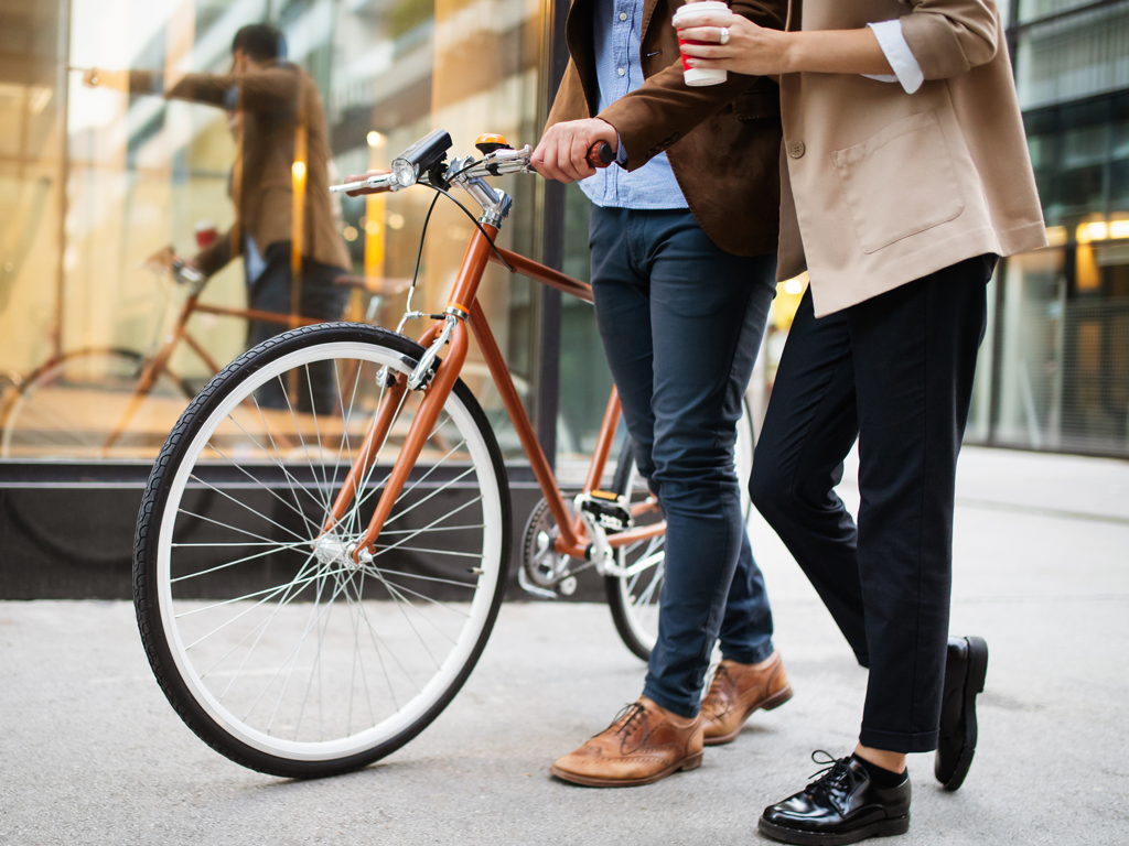 to mænd går og taler med en kaffe i hånden. Den ene mand har en cykel med sig