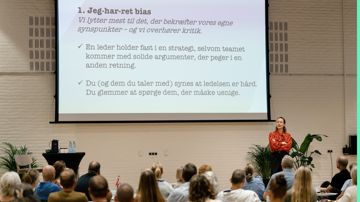 Oplægsholder Signe Biering fortæller om bias der bøvler foran nogle tillidsrepræsentanter der sidder med ryggen til. 