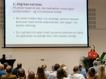 Oplægsholder Signe Biering fortæller om bias der bøvler foran nogle tillidsrepræsentanter der sidder med ryggen til.
