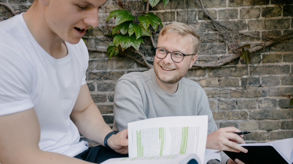 to drenge læser i deres studiebøger og smiler