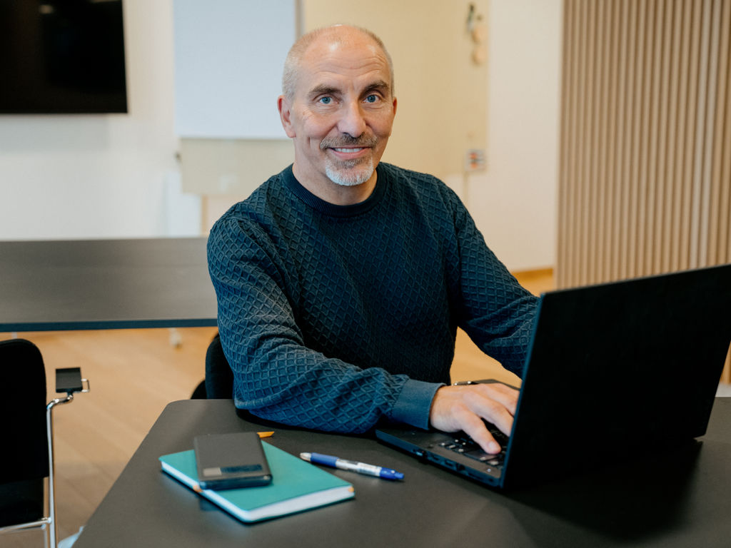 Mand sidder og smiler foran computer