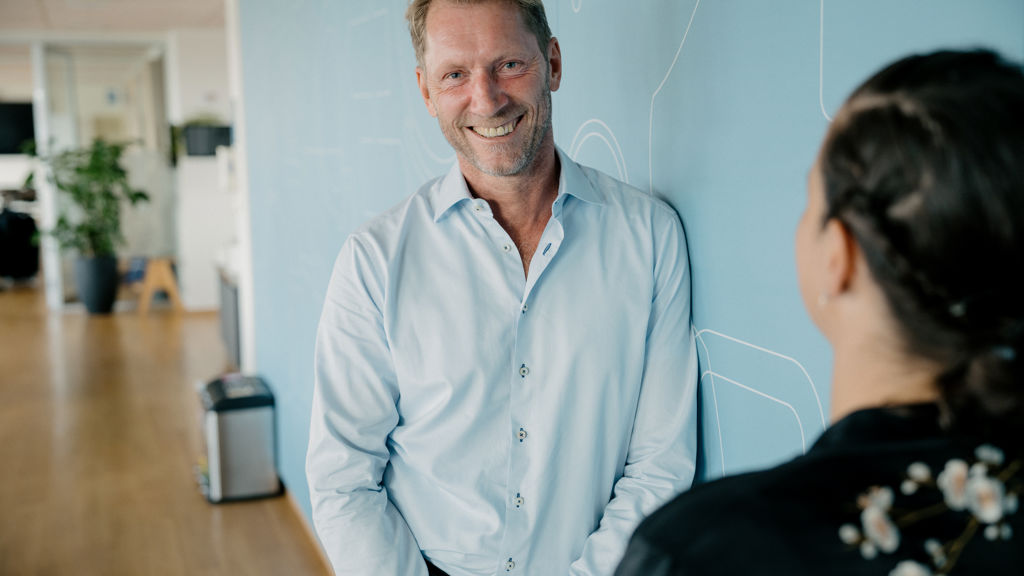 Smilende mand læner sig op af blå væg 