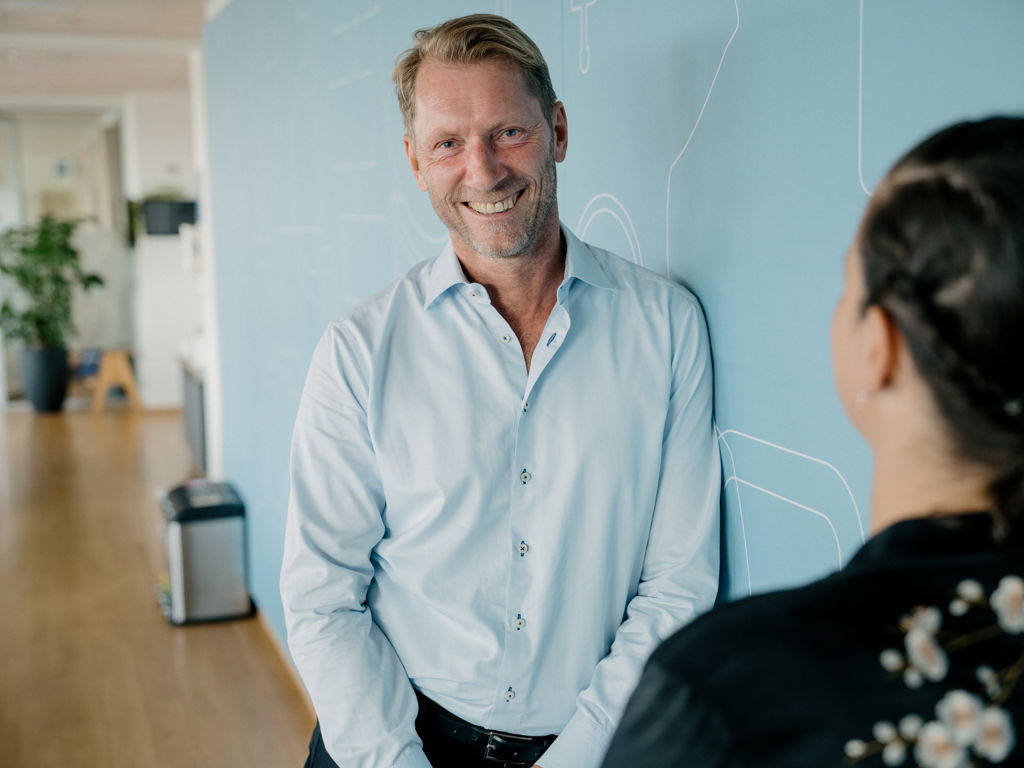 Smilende mand læner sig op af blå væg 