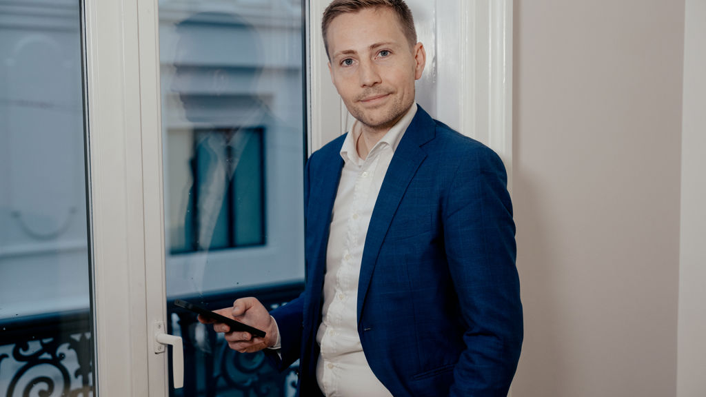 Mand står ved vindue med mobil i hånden