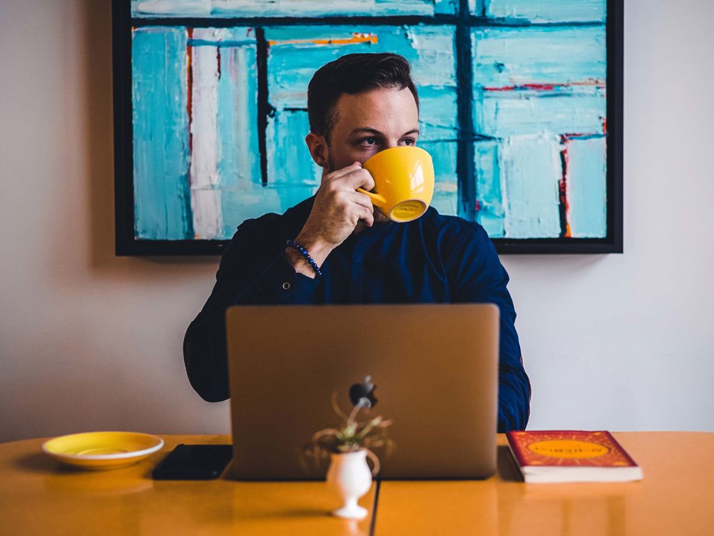 ung mand sidder ved sin computer og drikker kaffe