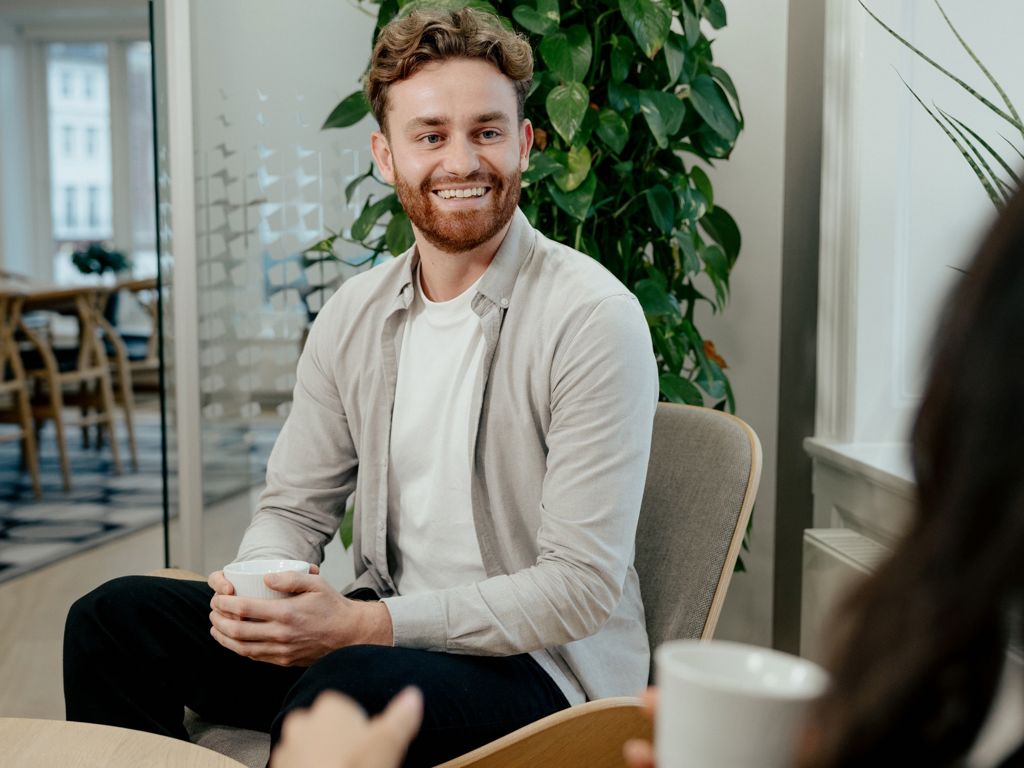 mand smiler stort med kaffekop i hånden