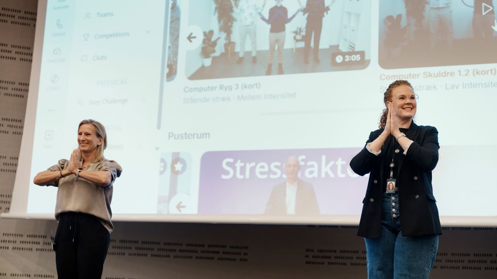 To kvinder står i forgrunden med hænderne samlet foran kroppen. I baggrunden ses en side fra hjemmeside.