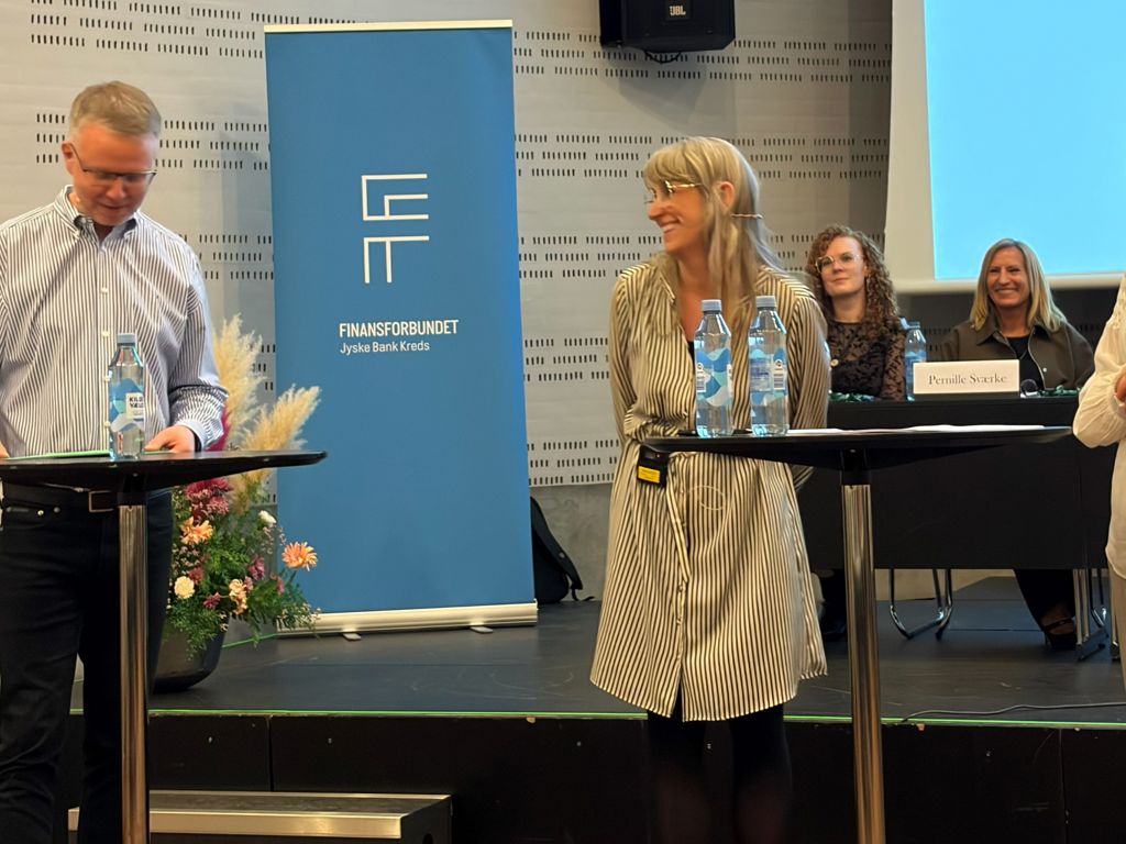 En mand interviewer to kvinder. de står foran to borde. I baggrunden ses to siddende kvinder.