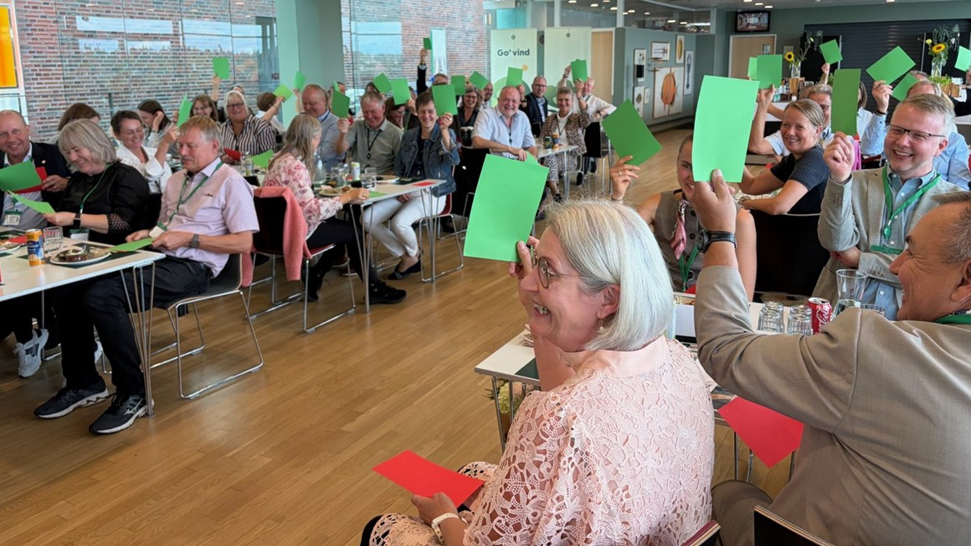 Menneskemængde sidder ved borde med grønne kort rakt op i luften