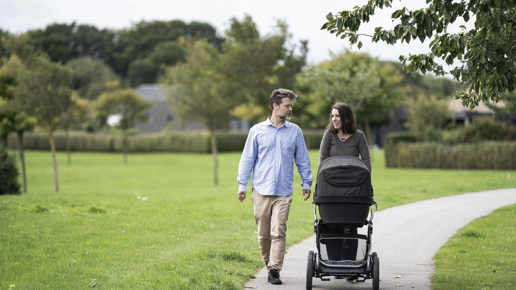 En mand og kvinde går med barnevogn i grønne omgivelser