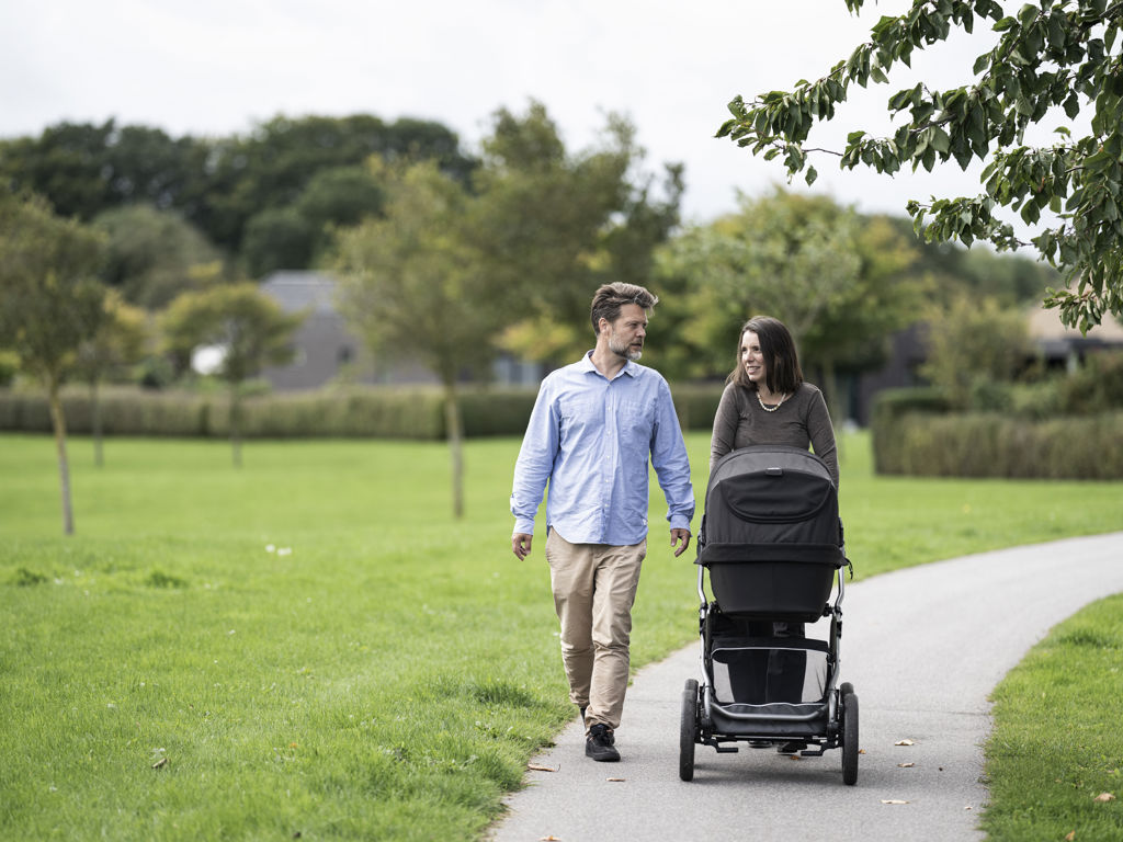 En mand og kvinde går med barnevogn i grønne omgivelser