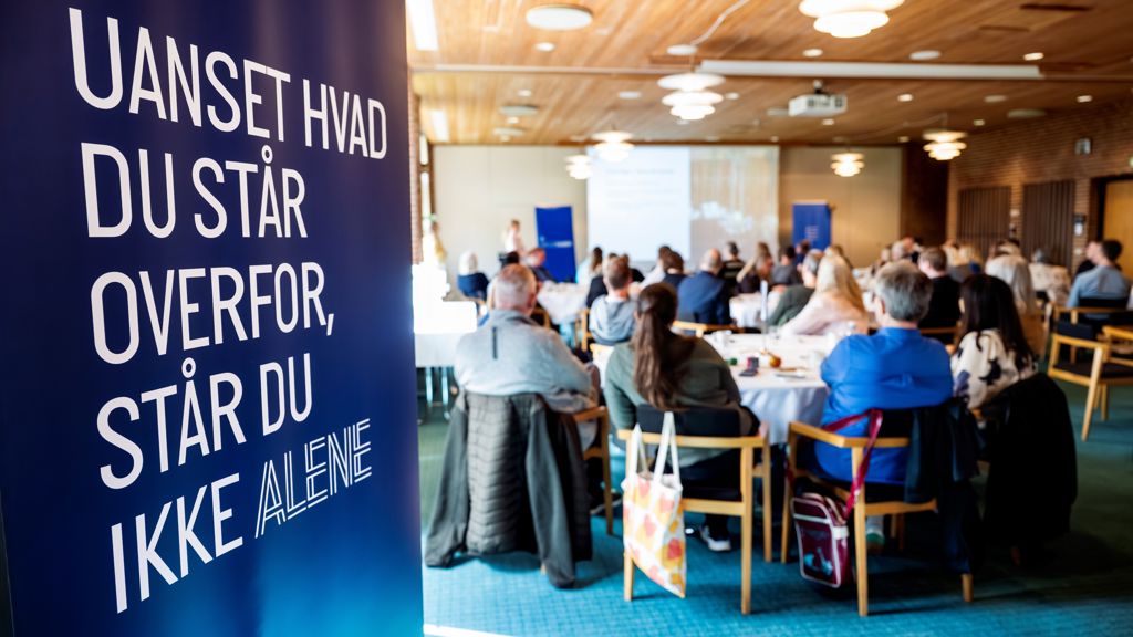 Gruppe fra ryggen med et banner hvor der er Uanset hvad du står overfor står du aldrig alene