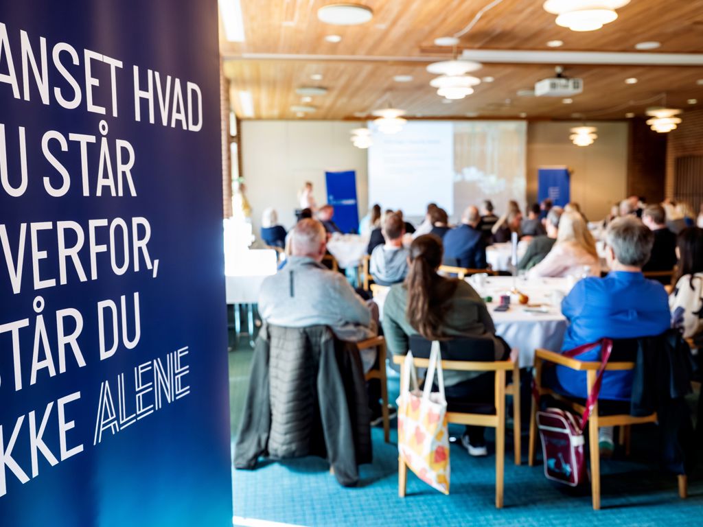 Gruppe fra ryggen med et banner hvor der er Uanset hvad du står overfor står du aldrig alene