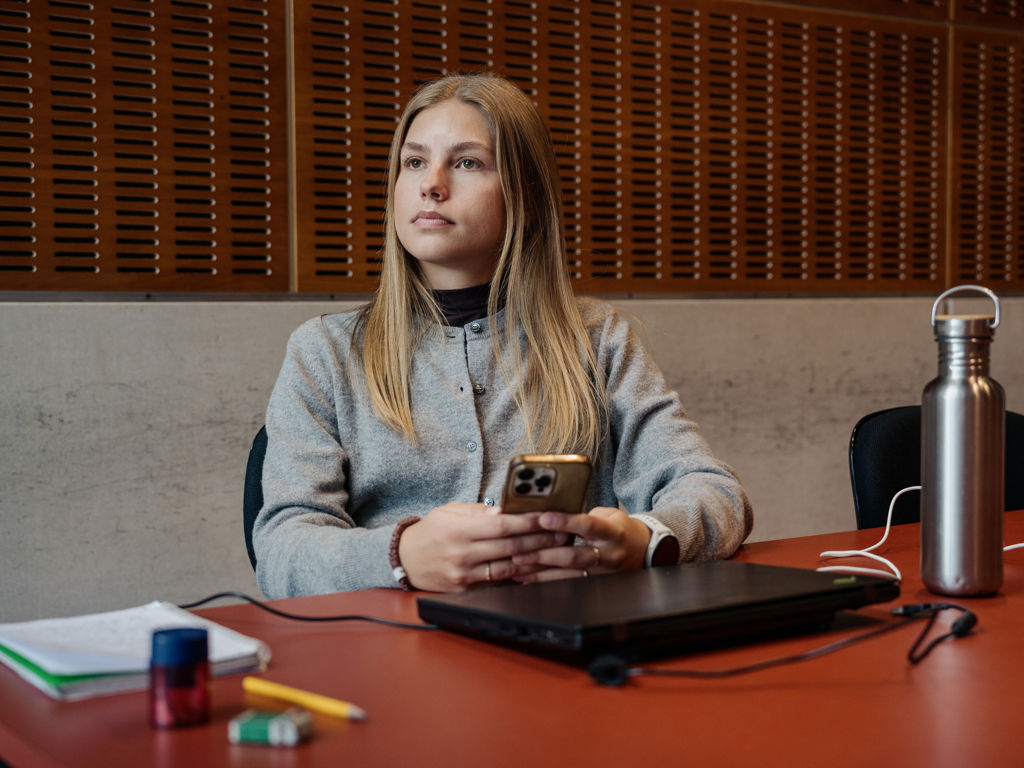 Ung pige sidder med sin tlf ved bord