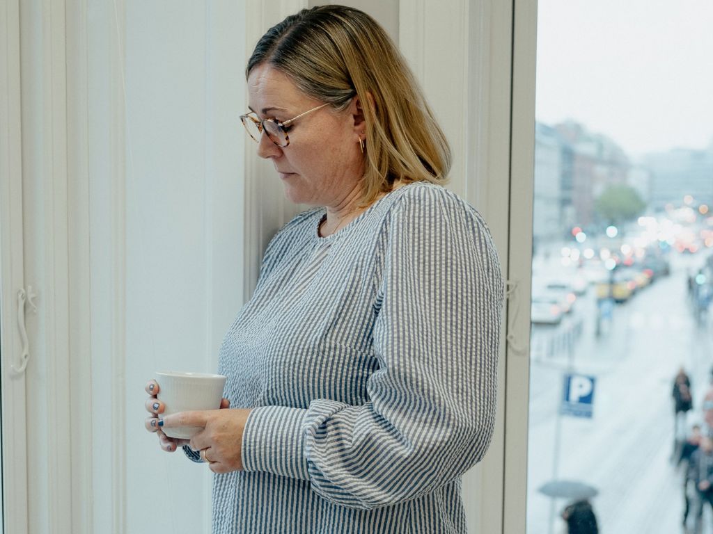 Kvinde står ved vindue med en kop kaffe