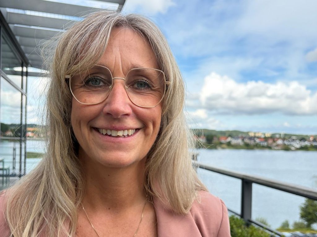 Portræt af smilende kvinde med vand i baggrunden.