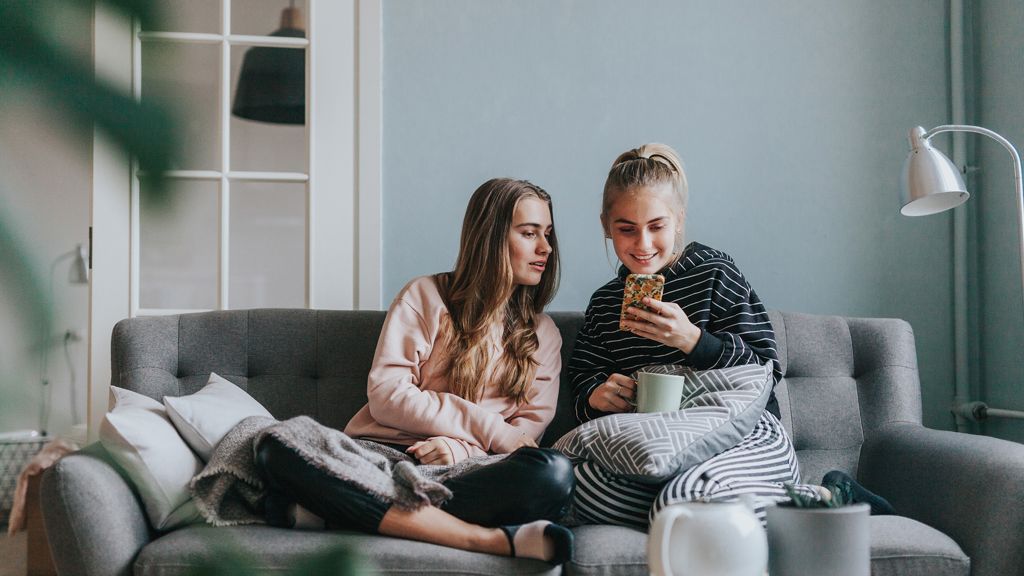 to unge kvinder sidder i en sofa og kigger på en mobil